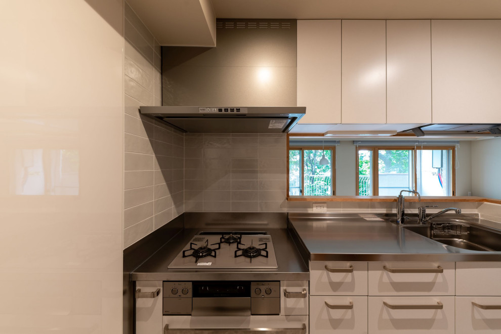 Design ideas for a mid-sized single-wall separate kitchen in Tokyo with an undermount sink, beaded inset cabinets, white cabinets, stainless steel benchtops, grey splashback, ceramic splashback, medium hardwood floors, no island, brown floor and wallpaper.