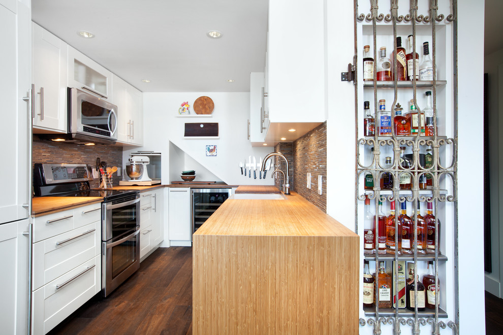 This is an example of a mid-sized transitional galley separate kitchen in Vancouver with a farmhouse sink, shaker cabinets, white cabinets, wood benchtops, brown splashback, stainless steel appliances, mosaic tile splashback, dark hardwood floors, a peninsula and brown floor.
