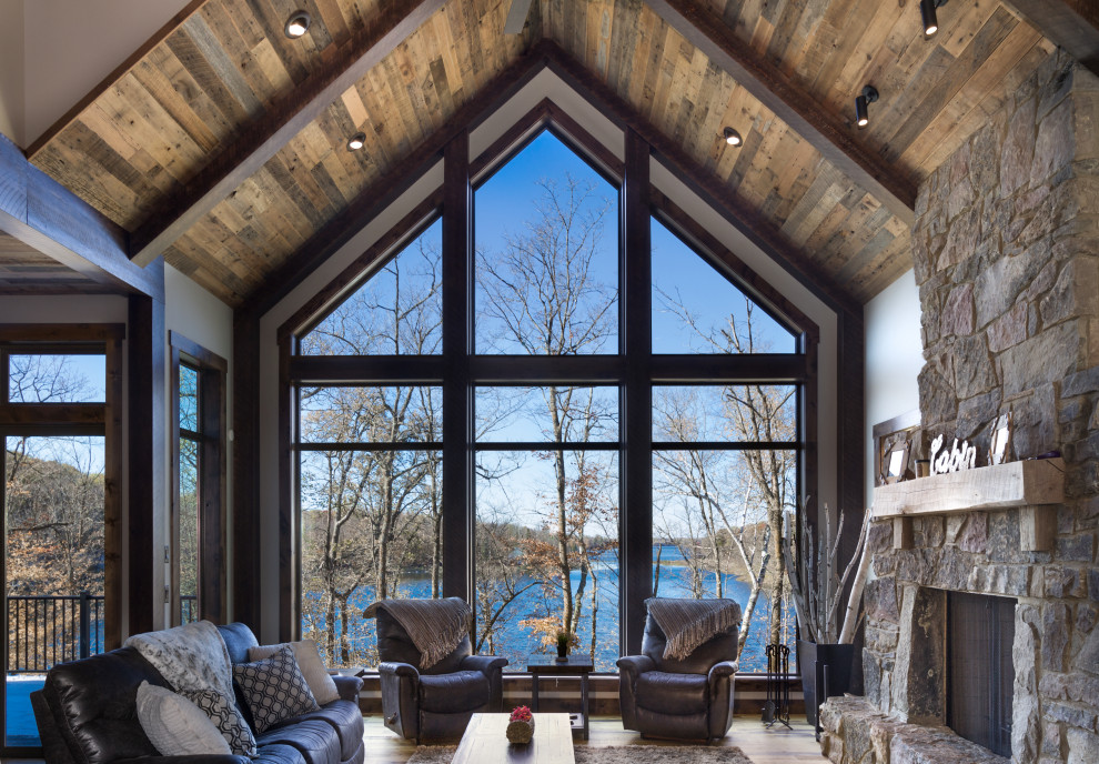Cette image montre un salon chalet avec un sol en bois brun, une cheminée standard, un manteau de cheminée en pierre et un plafond en bois.
