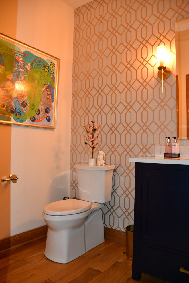 Example of a small minimalist medium tone wood floor, brown floor and wallpaper powder room design in Milwaukee with flat-panel cabinets, blue cabinets, a two-piece toilet, beige walls, an undermount sink, quartz countertops, beige countertops and a freestanding vanity