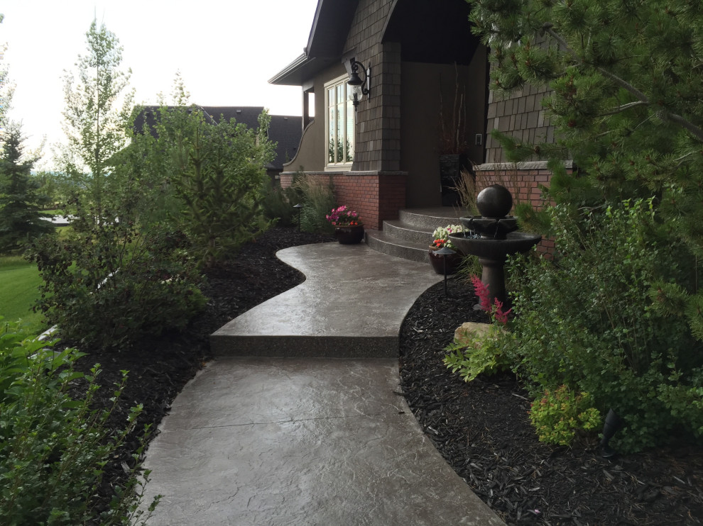 This is an example of a large traditional front yard garden in Calgary with with path and concrete pavers.