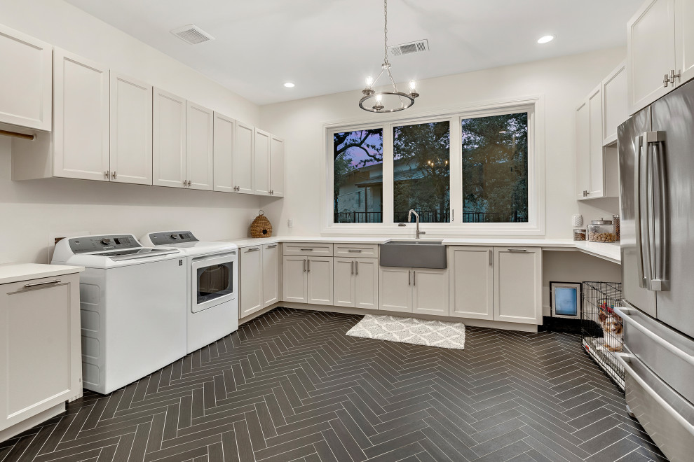 Photo of an expansive mediterranean u-shaped utility room in Austin with a farmhouse sink, recessed-panel cabinets, grey cabinets, white walls, black floor and white benchtop.