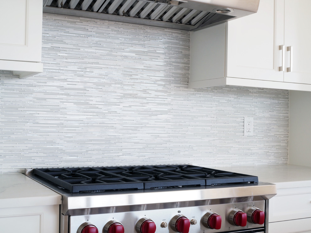 Eat-in kitchen - mid-sized transitional l-shaped light wood floor eat-in kitchen idea in New York with recessed-panel cabinets, white cabinets, quartz countertops, an island, an undermount sink, multicolored backsplash, glass tile backsplash and stainless steel appliances