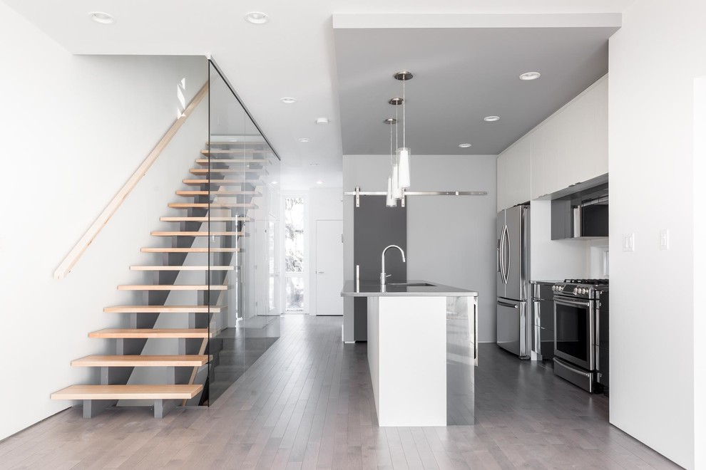 Mid-sized minimalist galley light wood floor and gray floor open concept kitchen photo in Edmonton with an undermount sink, flat-panel cabinets, gray cabinets, quartz countertops, window backsplash, stainless steel appliances and an island