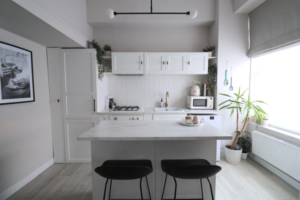 Exempel på ett litet modernt vit linjärt vitt kök med öppen planlösning, med en undermonterad diskho, skåp i shakerstil, vita skåp, laminatbänkskiva, vitt stänkskydd, stänkskydd i keramik, vita vitvaror, vinylgolv, en köksö och beiget golv