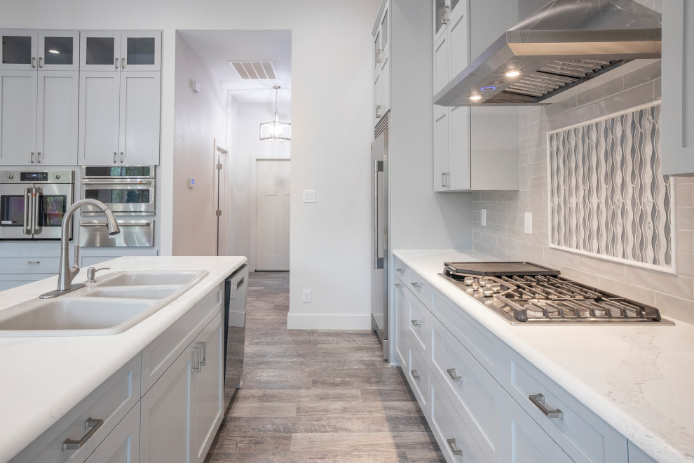 Design ideas for a large contemporary galley eat-in kitchen in Austin with grey cabinets, granite benchtops, grey splashback, glass tile splashback, multiple islands, white benchtop, a triple-bowl sink, shaker cabinets, stainless steel appliances, vinyl floors and grey floor.