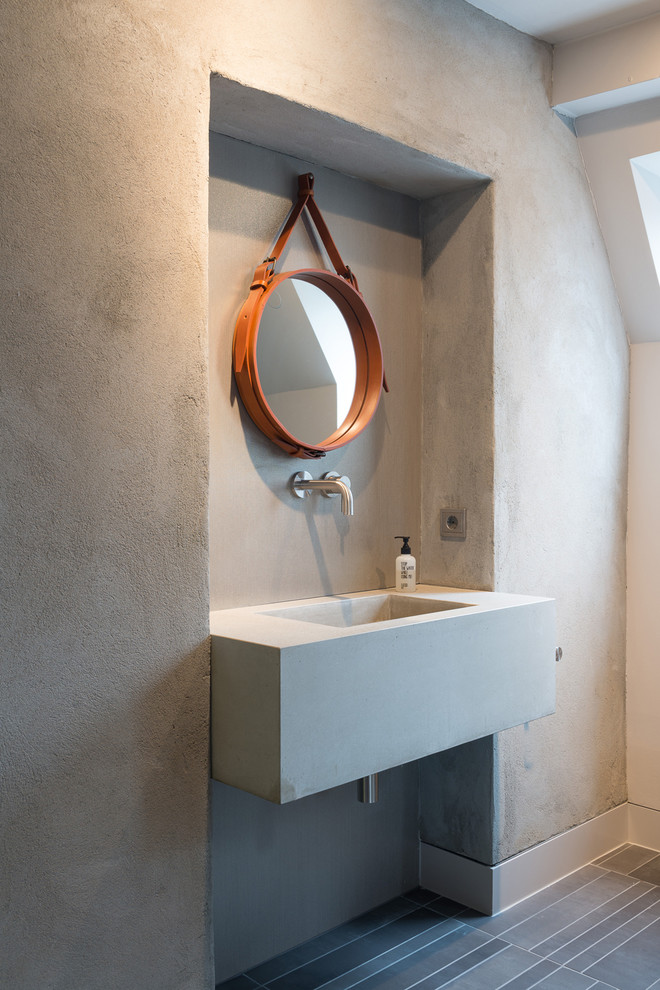 Photo of an industrial powder room in Berlin with grey walls, a wall-mount sink and concrete benchtops.