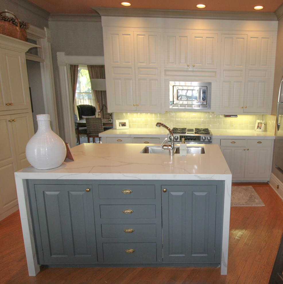 Kitchen - transitional medium tone wood floor and brown floor kitchen idea with an undermount sink, raised-panel cabinets, white cabinets, quartz countertops, white backsplash, ceramic backsplash, stainless steel appliances, an island and white countertops