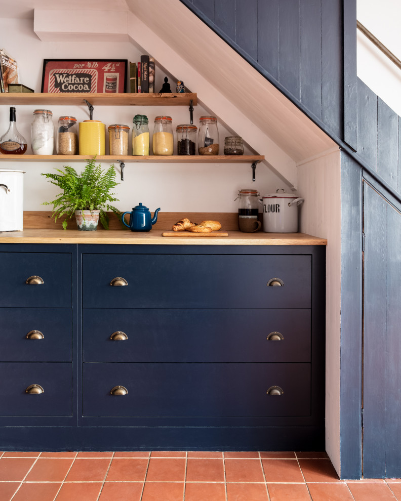 This is an example of a small traditional u-shaped eat-in kitchen in Other with a farmhouse sink, shaker cabinets, blue cabinets, wood benchtops, grey splashback, ceramic splashback, white appliances, terra-cotta floors and brown benchtop.