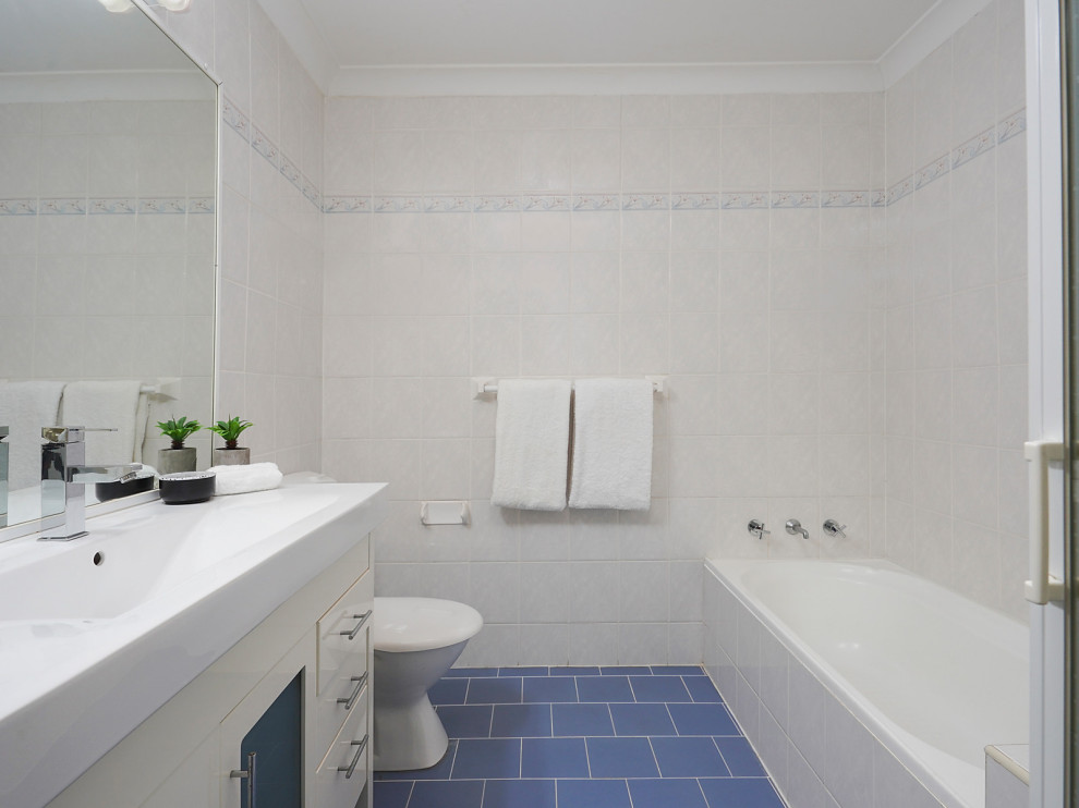 This is an example of a mid-sized contemporary master bathroom in Sydney with a one-piece toilet, beige tile, ceramic tile, ceramic floors, blue floor, white benchtops and a single vanity.