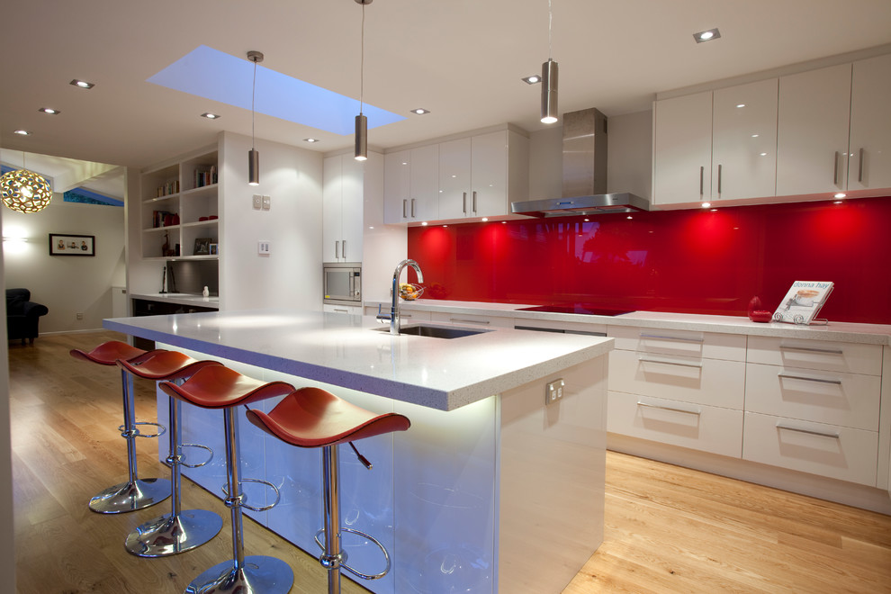 Modern kitchen in Auckland with red splashback, glass sheet splashback, an undermount sink, flat-panel cabinets, white cabinets and quartz benchtops.