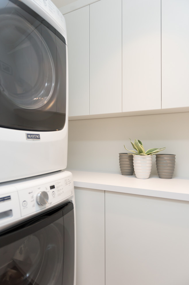 Small industrial galley dedicated laundry room in Vancouver with flat-panel cabinets, white cabinets, laminate benchtops, white walls, dark hardwood floors, a stacked washer and dryer, brown floor and white benchtop.