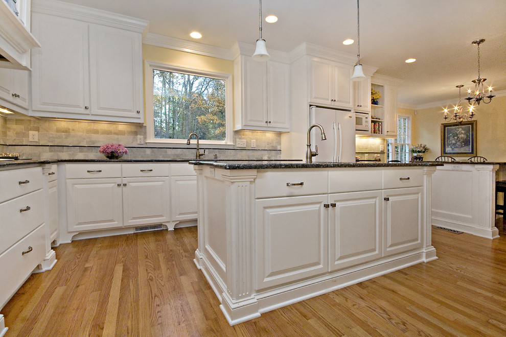 Inspiration for a large traditional l-shaped eat-in kitchen in Raleigh with an undermount sink, raised-panel cabinets, white cabinets, granite benchtops, white splashback, subway tile splashback, white appliances and multiple islands.