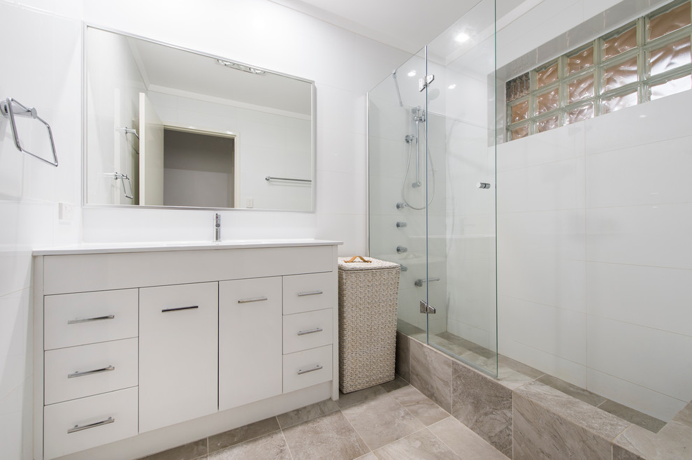 This is an example of a small contemporary 3/4 bathroom in Perth with flat-panel cabinets, white cabinets, solid surface benchtops, a shower/bathtub combo, white tile, ceramic tile, white walls and ceramic floors.