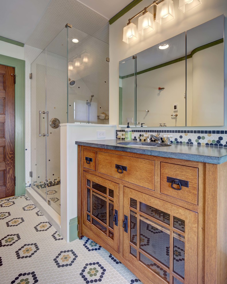 Inspiration for a mid-sized arts and crafts bathroom in New York with furniture-like cabinets, medium wood cabinets, a two-piece toilet, white tile, white walls, porcelain floors, an undermount sink, granite benchtops, multi-coloured floor, a hinged shower door and grey benchtops.