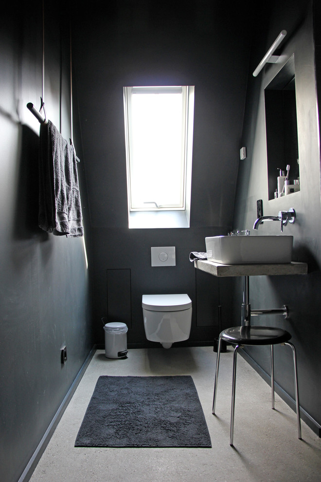 Photo of a small industrial powder room in Berlin with a vessel sink, a wall-mount toilet, black walls, concrete floors and concrete benchtops.