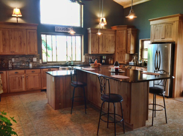 Example of a mountain style u-shaped eat-in kitchen design with a farmhouse sink, recessed-panel cabinets, light wood cabinets, granite countertops, multicolored backsplash, stainless steel appliances and an island