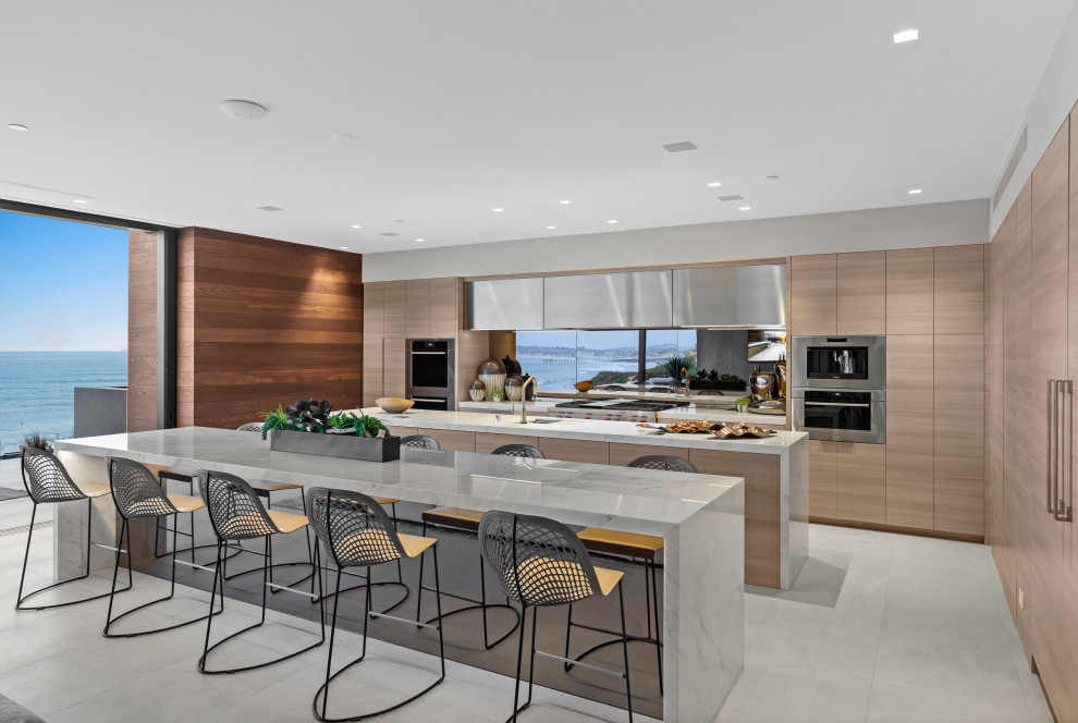 Photo of a large contemporary galley open plan kitchen in San Diego with a single-bowl sink, light wood cabinets, marble benchtops, glass sheet splashback, multiple islands, beige floor and white benchtop.