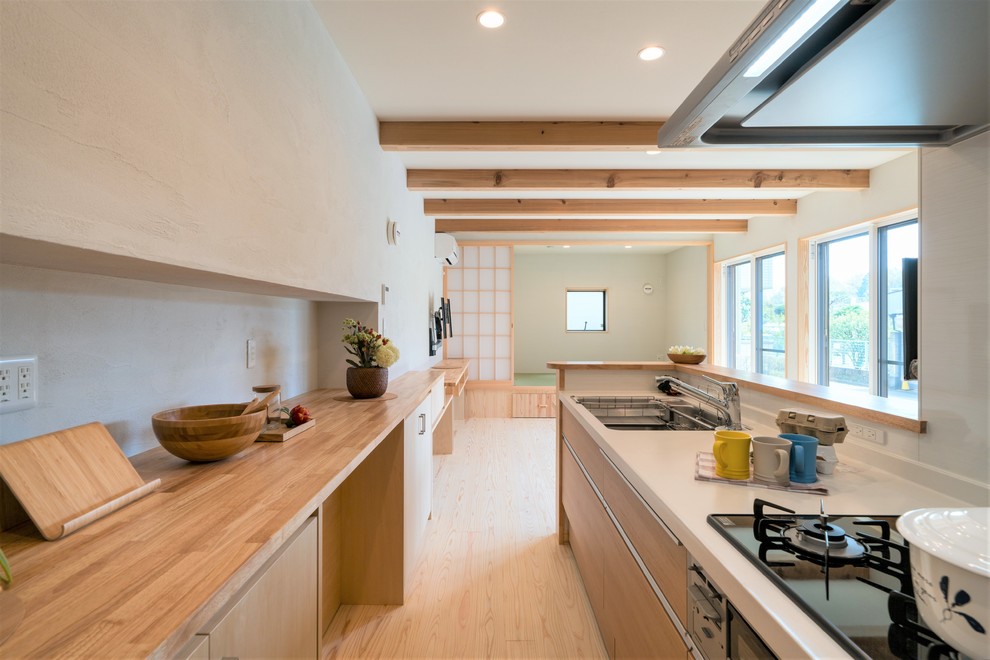 This is an example of an asian single-wall kitchen in Tokyo with a single-bowl sink, flat-panel cabinets, light wood cabinets, white splashback, light hardwood floors, a peninsula, beige floor and beige benchtop.