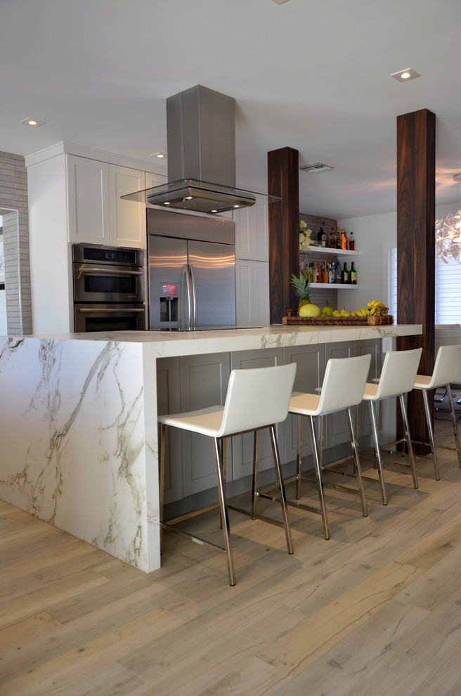 This is an example of a mid-sized beach style l-shaped open plan kitchen in Miami with a farmhouse sink, shaker cabinets, white cabinets, quartz benchtops, grey splashback, porcelain splashback, stainless steel appliances, porcelain floors and with island.