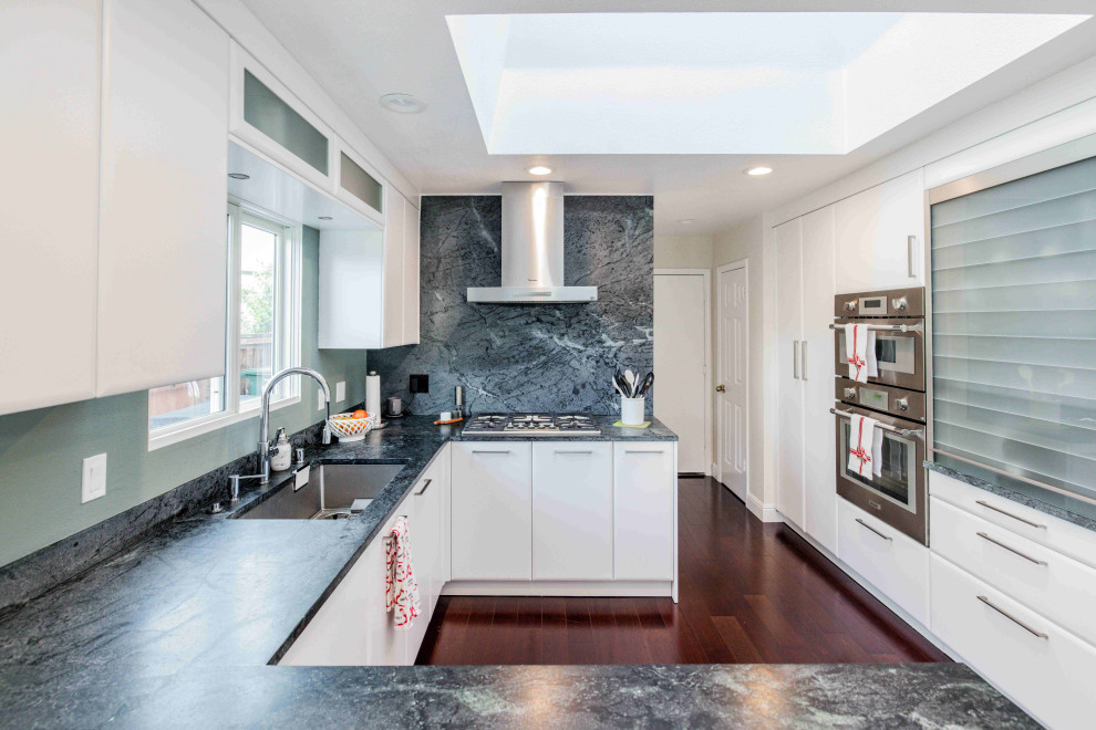 Mid-sized contemporary u-shaped kitchen pantry with an undermount sink, flat-panel cabinets, white cabinets, solid surface benchtops, black splashback, engineered quartz splashback, stainless steel appliances, dark hardwood floors, a peninsula, brown floor, black benchtop and recessed.
