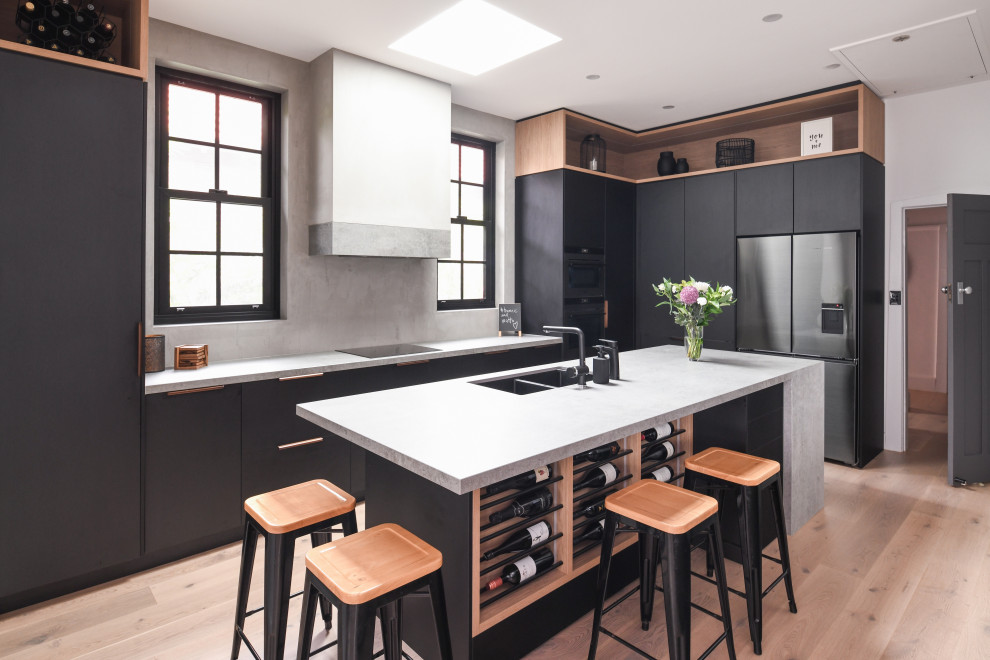 Inspiration for a large industrial l-shaped open plan kitchen in Sydney with an undermount sink, flat-panel cabinets, black cabinets, grey splashback, black appliances, light hardwood floors, with island, brown floor, grey benchtop and exposed beam.