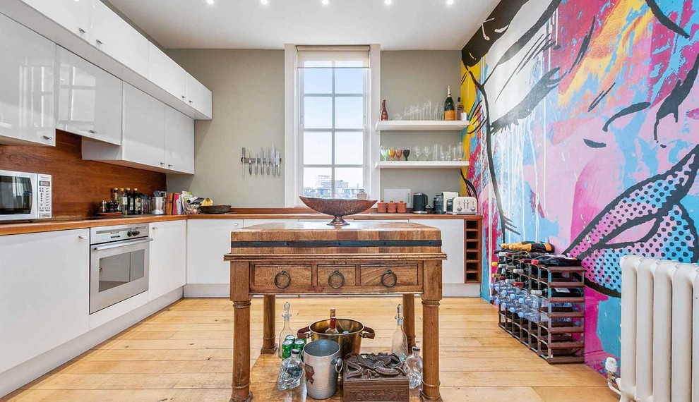 This is an example of a large eclectic l-shaped separate kitchen in London with flat-panel cabinets, white cabinets, wood benchtops, brown splashback, timber splashback, stainless steel appliances, medium hardwood floors, with island and yellow floor.