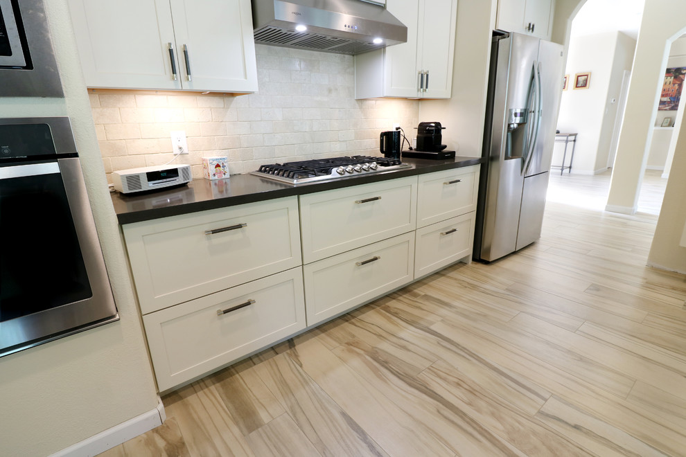 Eat-in kitchen - mid-sized transitional u-shaped porcelain tile and beige floor eat-in kitchen idea in Houston with an undermount sink, recessed-panel cabinets, white cabinets, soapstone countertops, white backsplash, subway tile backsplash, stainless steel appliances, an island and black countertops
