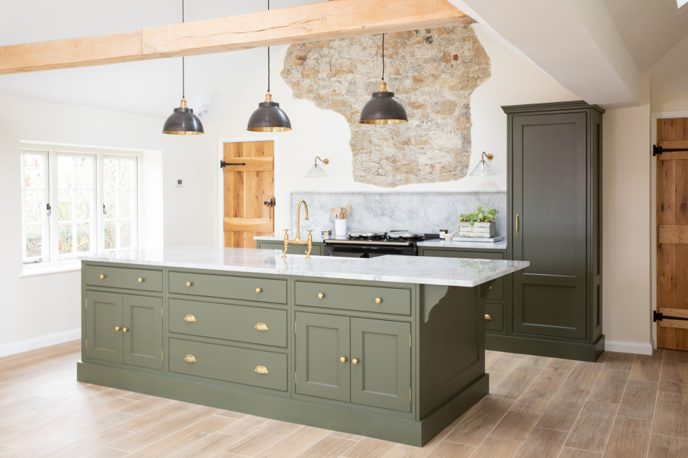 Traditional galley kitchen in Sussex with a farmhouse sink, beaded inset cabinets, green cabinets, grey splashback, stone slab splashback, black appliances, medium hardwood floors, with island, brown floor and grey benchtop.