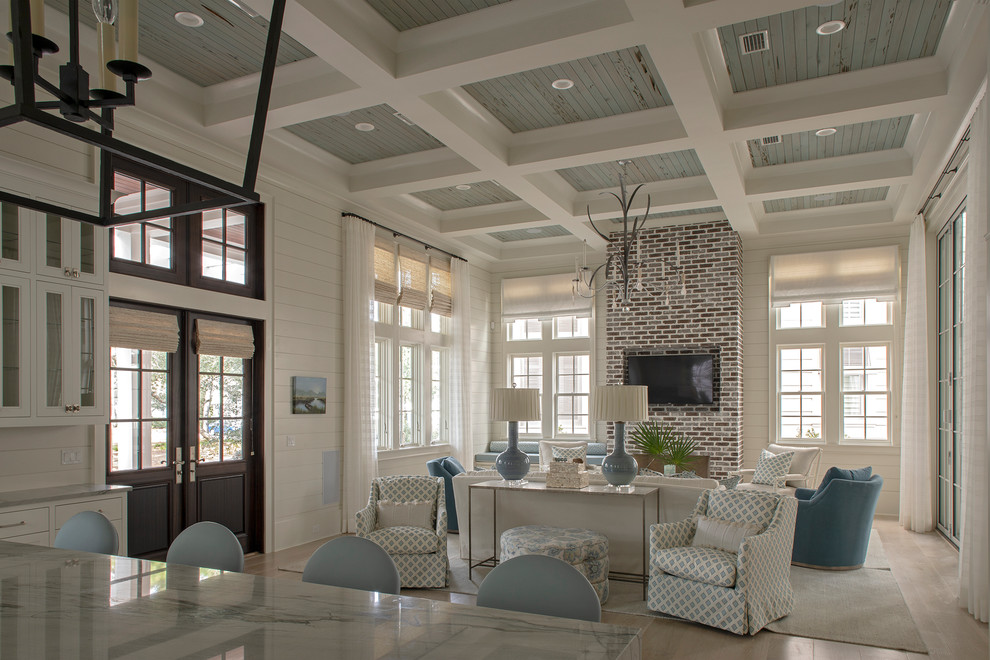 This is an example of a large beach style formal open concept living room in Other with white walls, medium hardwood floors, a standard fireplace, a brick fireplace surround, a wall-mounted tv and brown floor.