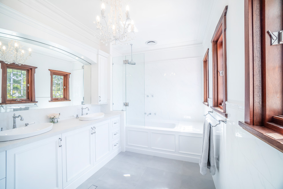 This is an example of a mid-sized traditional master bathroom in Perth with beaded inset cabinets, white cabinets, a drop-in tub, a shower/bathtub combo, white tile, ceramic tile, white walls, ceramic floors, a vessel sink, engineered quartz benchtops, grey floor and grey benchtops.
