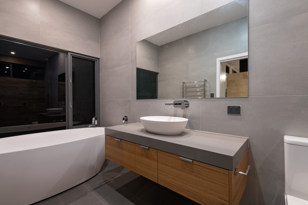 Design ideas for a mid-sized contemporary master bathroom in Adelaide with flat-panel cabinets, grey cabinets, a freestanding tub, a double shower, a one-piece toilet, gray tile, ceramic tile, grey walls, ceramic floors, a trough sink, engineered quartz benchtops, grey floor, an open shower, grey benchtops, a single vanity, a floating vanity and wood walls.