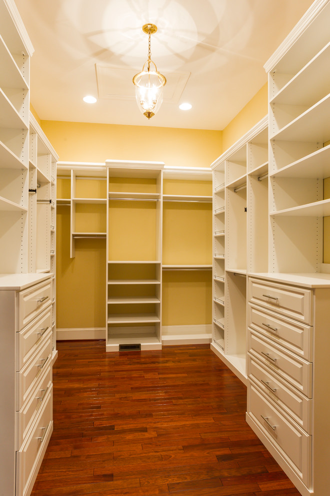 Large traditional gender-neutral walk-in wardrobe in Charlotte with white cabinets and dark hardwood floors.