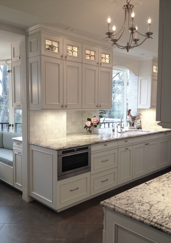 This is an example of a traditional kitchen in Seattle with an undermount sink, recessed-panel cabinets, white cabinets, granite benchtops, white splashback, stone tile splashback and porcelain floors.