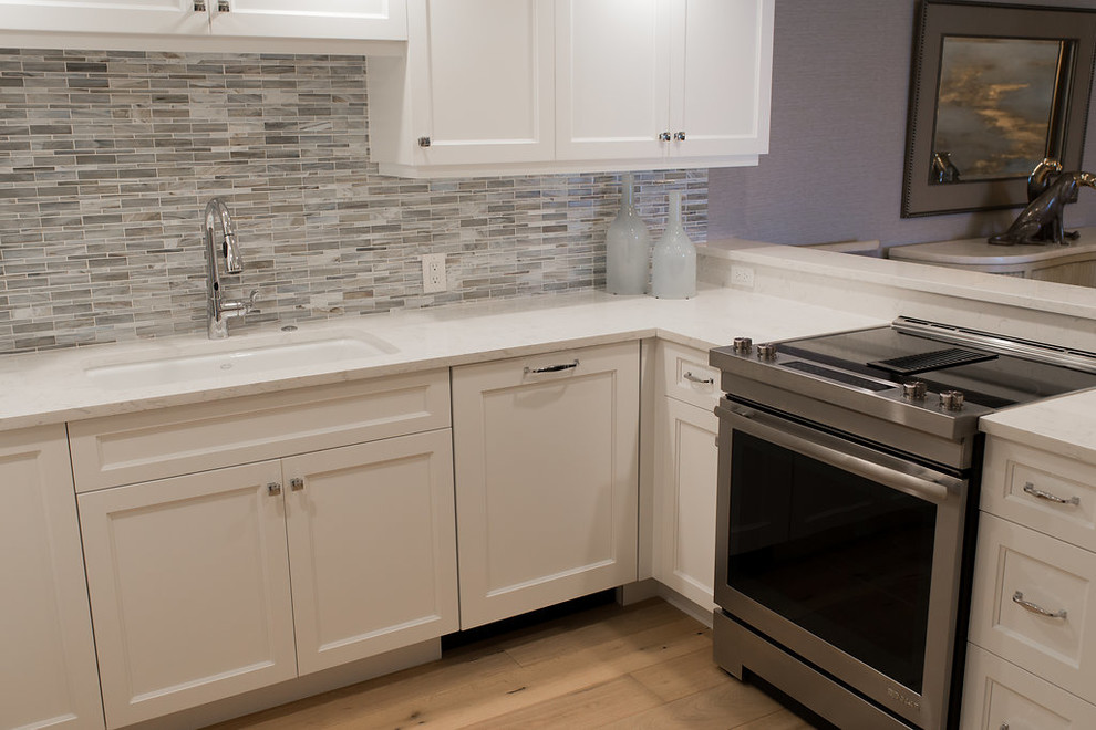 Small transitional u-shaped medium tone wood floor and brown floor eat-in kitchen photo in Miami with an undermount sink, white cabinets, stainless steel appliances, shaker cabinets, quartz countertops, multicolored backsplash, glass tile backsplash and no island