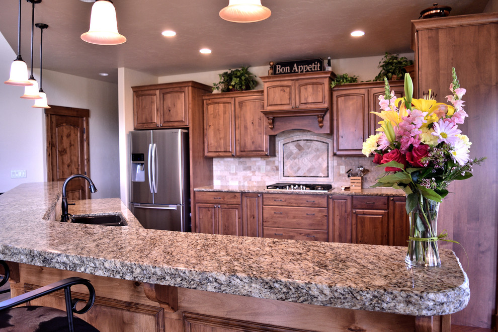 Example of a large mountain style galley medium tone wood floor and brown floor eat-in kitchen design in Denver with an undermount sink, medium tone wood cabinets, granite countertops, beige backsplash, stone tile backsplash, stainless steel appliances, an island and raised-panel cabinets