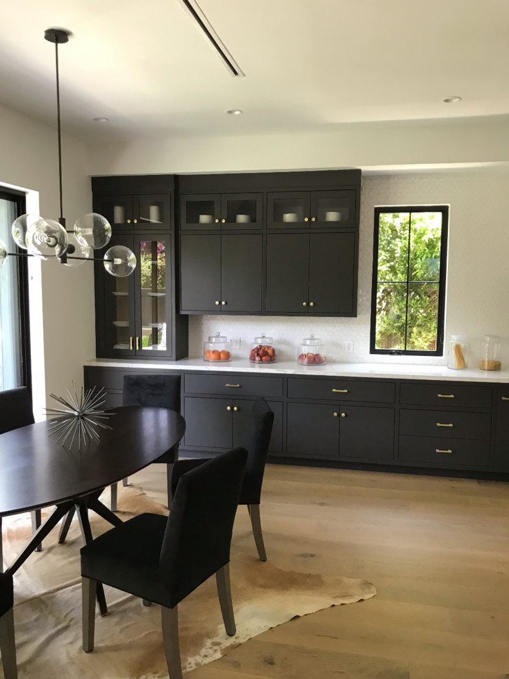 Photo of a large country l-shaped open plan kitchen in Los Angeles with glass-front cabinets, white splashback, ceramic splashback, stainless steel appliances, light hardwood floors, with island, white benchtop, a farmhouse sink, white cabinets, quartzite benchtops, brown floor, exposed beam and timber.