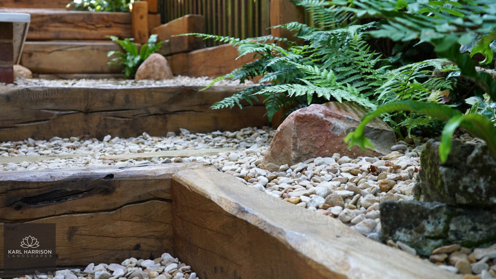 Aménagement d'un petit jardin latéral montagne l'été avec une exposition partiellement ombragée, des pavés en pierre naturelle et une clôture en bois.