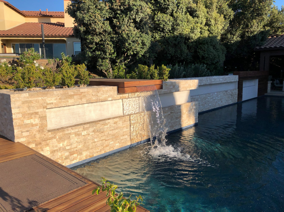 This is an example of a mid-sized contemporary backyard rectangular lap pool in San Diego with a water feature and decking.