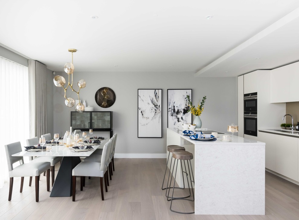 Inspiration for a contemporary eat-in kitchen in London with an undermount sink, flat-panel cabinets, white cabinets, brown splashback, black appliances, light hardwood floors, with island and beige floor.