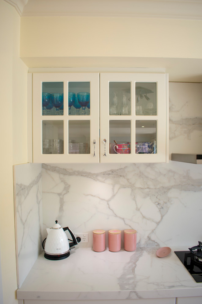 Design ideas for a mid-sized mediterranean u-shaped eat-in kitchen in Perth with a double-bowl sink, shaker cabinets, white cabinets, white splashback, stone slab splashback, stainless steel appliances, laminate floors, a peninsula, brown floor and white benchtop.