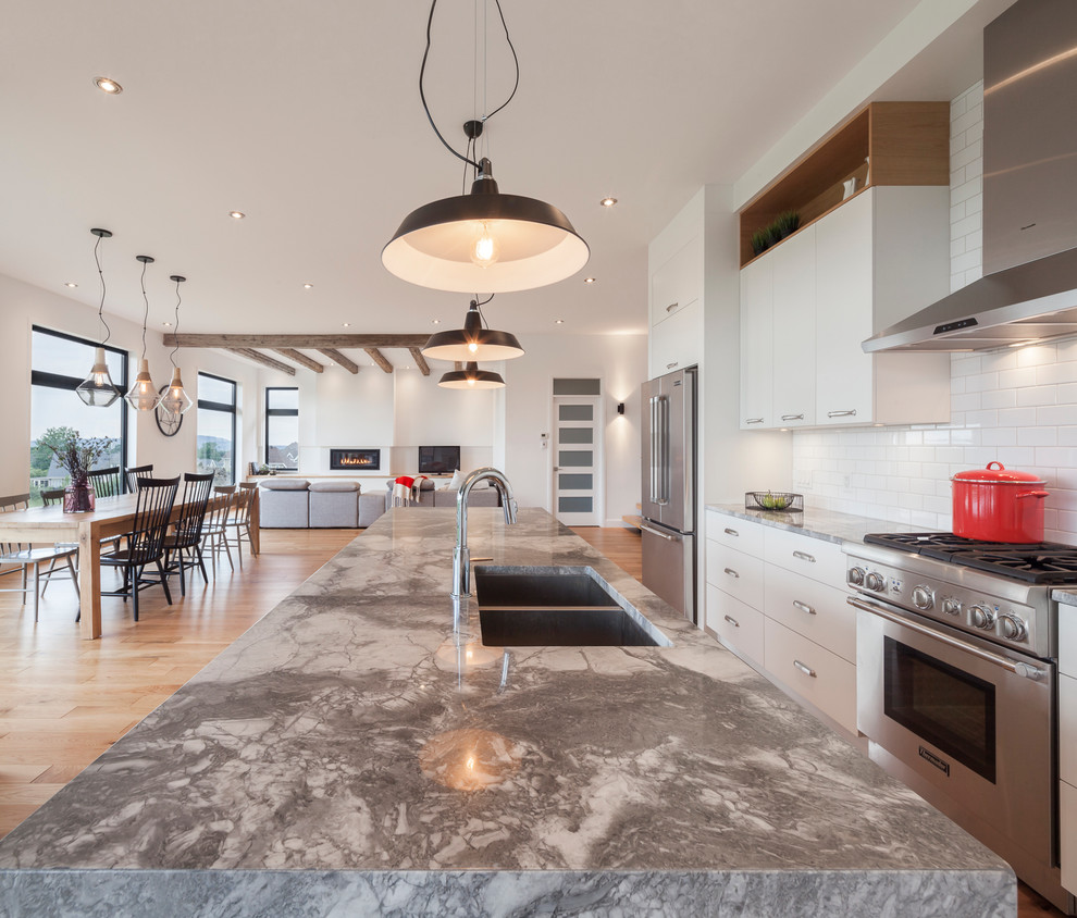 Design ideas for a contemporary l-shaped kitchen in Montreal with an undermount sink, flat-panel cabinets, white cabinets, quartzite benchtops, white splashback, ceramic splashback, stainless steel appliances, light hardwood floors and with island.