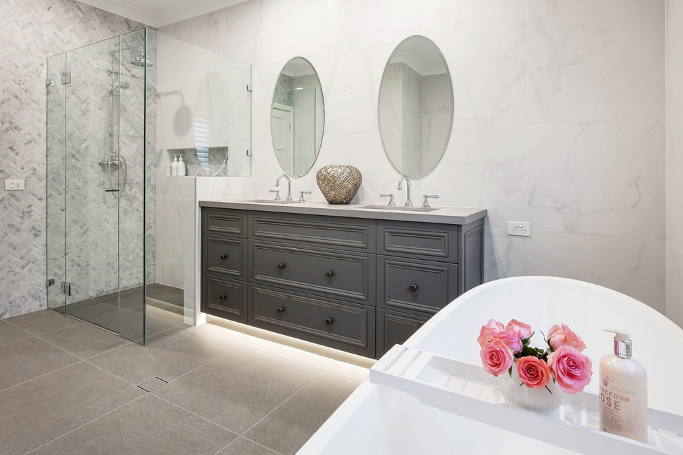Inspiration for a mid-sized traditional 3/4 bathroom in Sydney with furniture-like cabinets, grey cabinets, a freestanding tub, an open shower, a one-piece toilet, white tile, marble, white walls, porcelain floors, an undermount sink, engineered quartz benchtops, grey floor, a hinged shower door and grey benchtops.