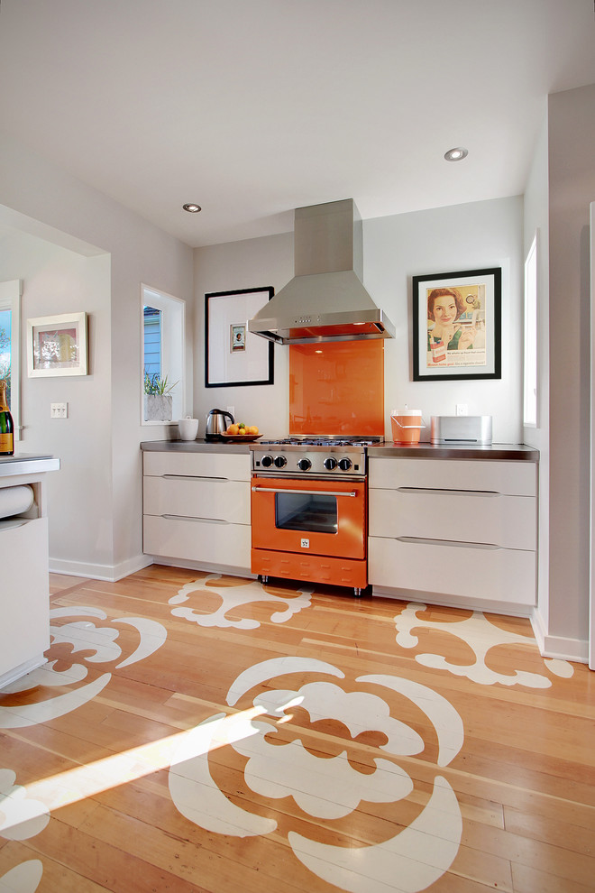 Photo of a contemporary separate kitchen in Seattle with flat-panel cabinets, white cabinets, orange splashback, glass sheet splashback, coloured appliances, zinc benchtops, painted wood floors and multi-coloured floor.