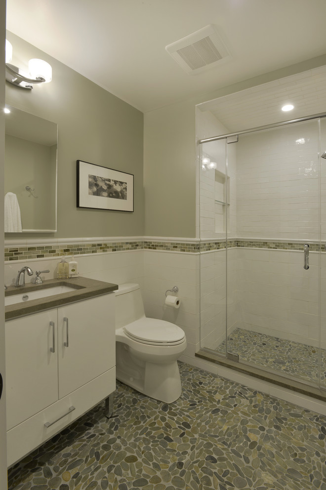 This is an example of a mid-sized transitional 3/4 bathroom in New York with furniture-like cabinets, white cabinets, an alcove shower, a one-piece toilet, white tile, porcelain tile, grey walls, pebble tile floors, an undermount sink, soapstone benchtops, green floor and a hinged shower door.