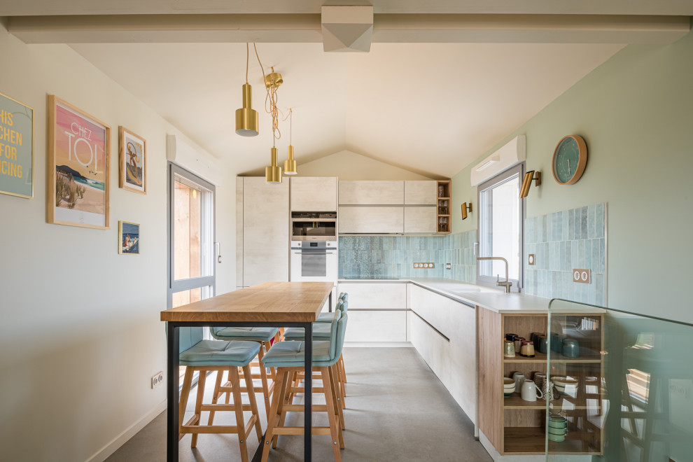 Cette image montre une petite cuisine marine en L et bois clair avec un placard à porte plane, une crédence bleue, un électroménager blanc, îlot, un sol gris et un plafond voûté.