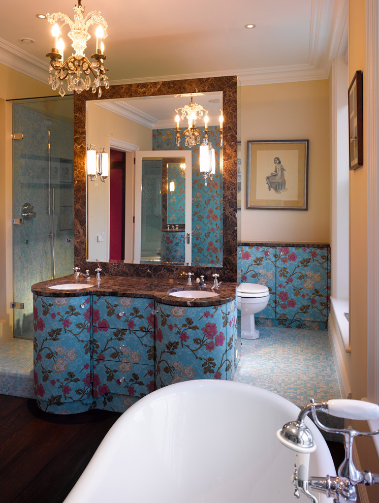 Photo of a mid-sized eclectic master bathroom in London with furniture-like cabinets, blue cabinets, a freestanding tub, an open shower, a one-piece toilet, blue tile, mosaic tile, beige walls, mosaic tile floors, an undermount sink, marble benchtops, blue floor, a hinged shower door, brown benchtops, a niche, a double vanity, a freestanding vanity and wallpaper.