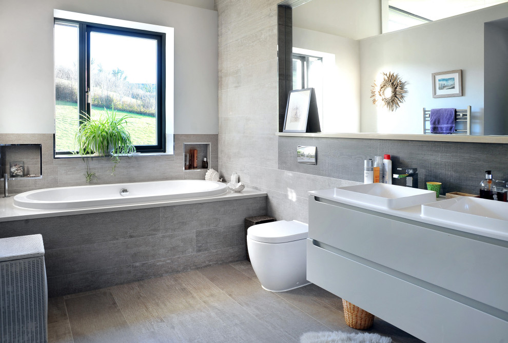 Photo of a mid-sized modern kids bathroom in Devon with flat-panel cabinets, grey cabinets, a drop-in tub, a one-piece toilet, gray tile, wood-look tile, grey walls, wood-look tile, a drop-in sink, grey floor, white benchtops, a double vanity and a floating vanity.