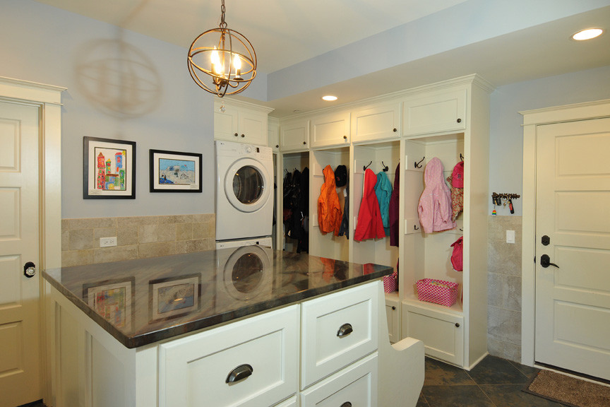 This is an example of a large transitional utility room in Chicago with recessed-panel cabinets, white cabinets, quartzite benchtops, blue walls, ceramic floors and a stacked washer and dryer.