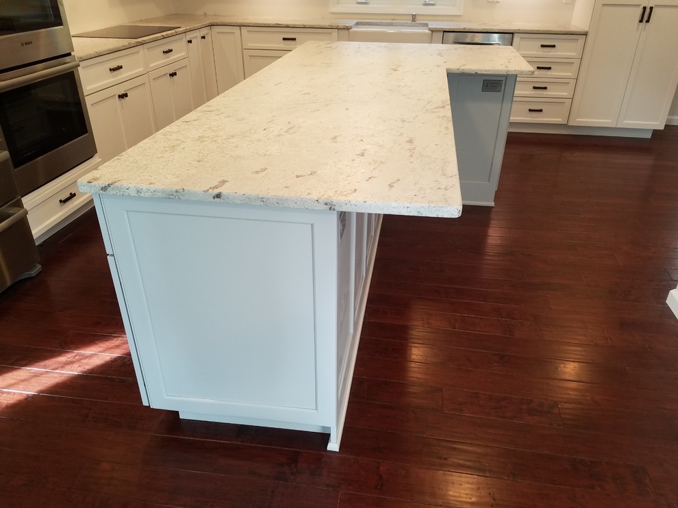 Example of a mid-sized transitional l-shaped dark wood floor and brown floor eat-in kitchen design with a farmhouse sink, shaker cabinets, white cabinets, granite countertops, white backsplash, subway tile backsplash, stainless steel appliances and an island